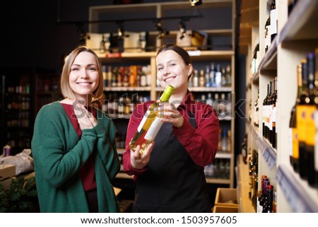 Picture of young women with bottle of wine in hands in store