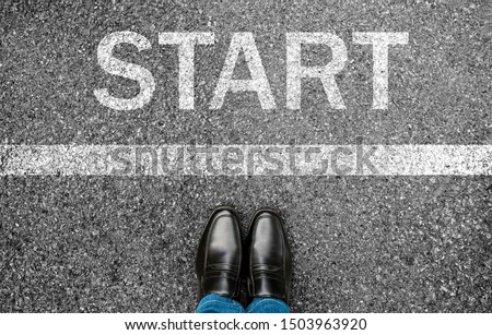 Business man standing on grunge concrete with white race line beginning idea. Top view. Feet and black shoes with word start written for concept on tarmac road background. Businessman challenge. Royalty-Free Stock Photo #1503963920