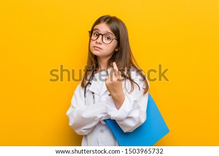 Little caucasian girl wearing a doctor costume pointing with finger at you as if inviting come closer.