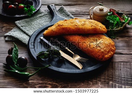 Tasty italian calzone pizza with fresh ingredients and vegetables on a black serving board. Wooden rustic background, dark style.
