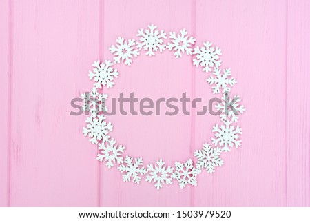 Holiday round frame made of christmas white snowflakes on pink wooden background. Composition with place for text. Flat lay, top view