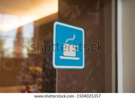 Close up to sticker of symbol coffee shop on glass background. Cafe wallpaper view. sticker on the window with a picture of a cup of coffee. coffee bar sticker on a glass blue