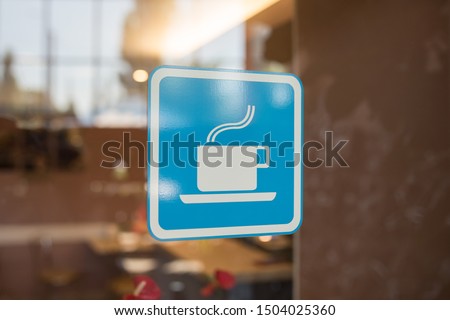 Close up to sticker of symbol coffee shop on glass background. Cafe wallpaper view. sticker on the window with a picture of a cup of coffee. coffee bar sticker on a glass blue