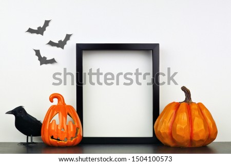 Mock up black frame with Jack o Lantern, pumpkin and crow decor on a shelf or desk. Halloween concept. Portrait frame against a white wall with bats.