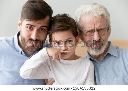 Happy funny multi 3 three generation men family close up portrait, cute child boy son grandson holding finger fake drawn moustache posing with young grown father and old grandfather look at camera Royalty-Free Stock Photo #1504135022