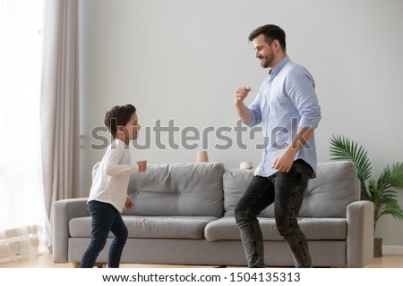 Happy active family young dad and cute little kid son dancing having fun in living room together, funny preschool small boy laughing imitating father moves, daddy child play at home leisure lifestyle