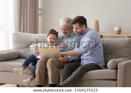 Happy three 3 age multi generation men family old grandfather young adult grown son father and child boy grandson having fun using laptop computer spend time browsing internet at home sit on sofa Royalty-Free Stock Photo #1504135523