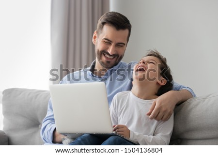 Cheerful male family happy dad and cute kid son bonding laughing watching funny cartoons comedy on laptop at home, smiling father hug small child boy having fun together using computer sit on sofa Royalty-Free Stock Photo #1504136804