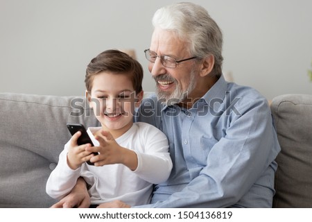 Happy senior grandfather and cute small grandson using smart phone apps at home, old grandpa embracing little grandchild holding looking at cellphone screen playing mobile game relaxing sit on sofa Royalty-Free Stock Photo #1504136819
