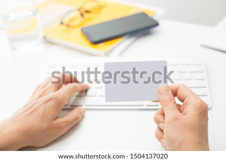 Blank white credit card mockup in hand on keyboard background.