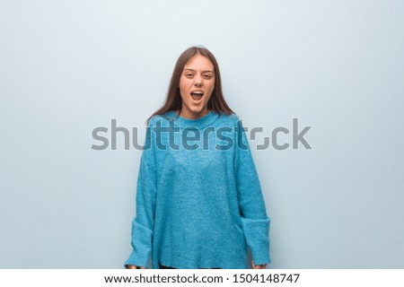 Young pretty woman wearing a blue sweater screaming very angry and aggressive