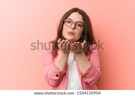 Young plus size business caucasian woman folding lips and holding palms to send air kiss.