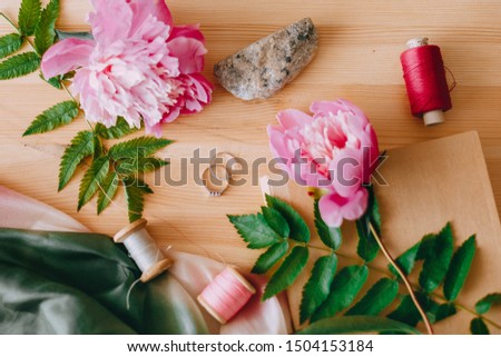 Wedding rings with peonies and leaves, sewing threads on a wooden table