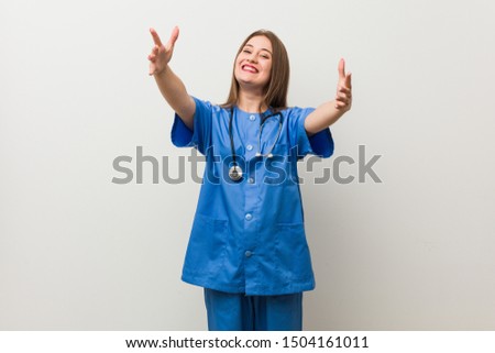 Young nurse woman against a white wall feels confident giving a hug to the camera.