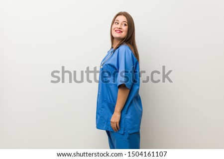 Young nurse woman against a white wall looks aside smiling, cheerful and pleasant.