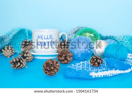 Cup with words Hello, winter, woolen scarf and Christmas ball on the blue background. 