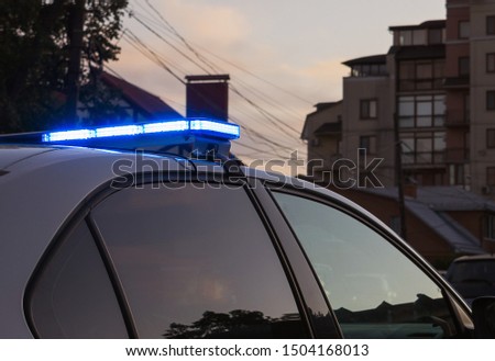 A part of an unrecognizable police car with a blue flasher on the roof, crime scene, night patrolling the city. 