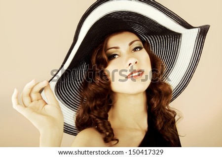 beautiful brunette with long curly hair in the dark swimsuit and the hat on the beach