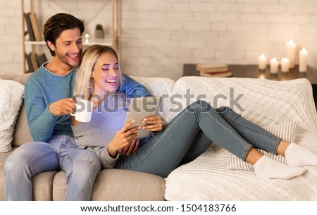 Cheerful Couple Using Tablet Computer Watching Film Relaxing On Sofa Indoor. Weekend Together