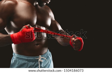 Marital arts concept. African american fighter wrapping red bandage on his hand, black studio background with copy space
