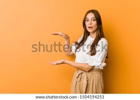 Young caucasian woman shocked and amazed holding a copy space between hands.