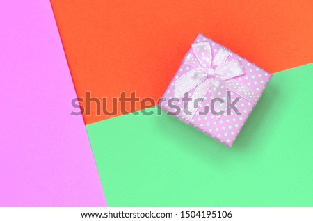 Small pink gift box lie on texture background of fashion pastel turquoise, red and pink colors paper
