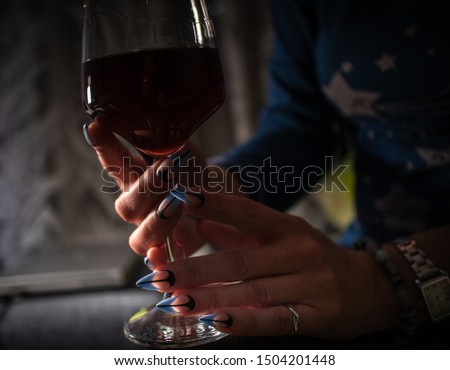 Woman with manicured nails holds glass of black wine