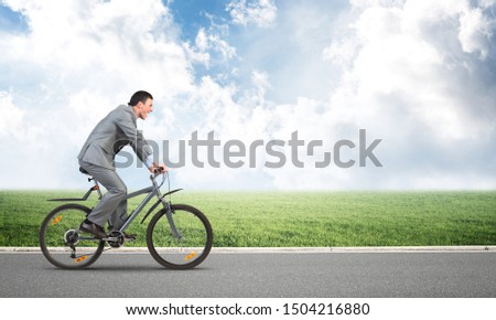 Businessman hurry to work by bike. Man wearing business suit riding bicycle on asphalt road. Handsome cyclist on background of blue sky. Nature landscape with copy space. Eco-friendly transport.