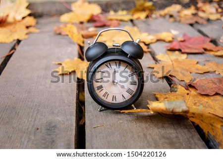 Vintage black alarm clock on autumn leaves. Time change abstract photo. Daylight saving time. Royalty-Free Stock Photo #1504220126