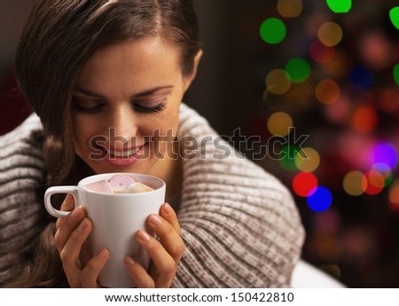 Happy woman with cup of hot chocolate with marshmallow in front of christmas lights