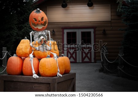 Pumpkin head skeleton holding s scary scarecrow doll with blank sign on Halloween