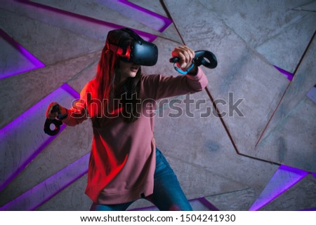 Use a sword. A young woman in a virtual helmet uses controllers in both hands, like the arms of virtual swords. She is actively fighting in a virtual battle.