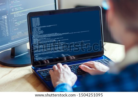 Back view of man freelancer is working on laptop at home office. Programmer developer is writing program code software on multiple computer screens. Remote work. Geek workplace concept. Royalty-Free Stock Photo #1504251095