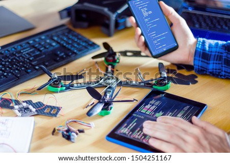 Closeup programmer hand holding smartphone and tablet with program code of software on screen for controlling FPV - first person view drone. Building quadcopter from kit with microcontrollers. Royalty-Free Stock Photo #1504251167