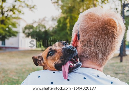 Human and dog friendship: young man hugs his funny dog, person's back perspective. Smiling puppy with floppy ears and tongue interacting with her owner Royalty-Free Stock Photo #1504320197