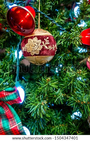 Decorative Christmas bauble and red bell hanging from an artificial pine tree. Part of a home decoration complete with lights. Ushers in the spirit and joy of Christmas.