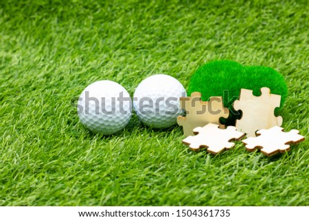 Golf ball and jigsaw are on green grass with love 