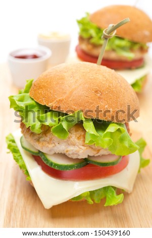 chicken burger with vegetables, cheese, ketchup and mustard on a wooden board, close-up, vertical