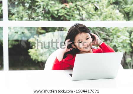A 6 year old Asian girl wearing a red chirt Watching a cartoons From a notebook with fun and happy On White table and blur background, concept to children and communication technology.