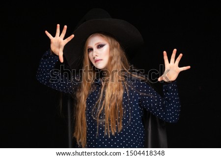 Halloween. Witch with a spider on his hat on black background Casts a spell with his hands. Beautiful young surprised woman in witches hat and costume holding. Wide Halloween party art design. Copy
