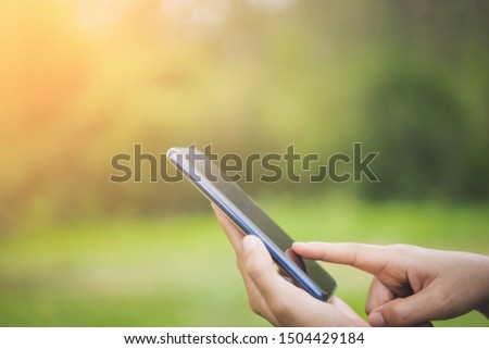 Woman hand using smart phone at outdoor nature park with sunset sky abstract background. Copy space technology business and travel nature holiday concept. Vintage tone filter effect color style.