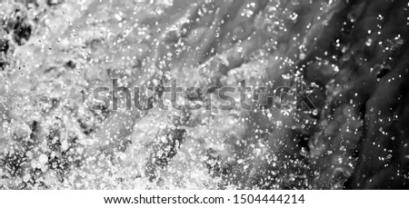 Close-up shot of splashing waterfall in rain season, bright drops and glittering particle motion. Monochrome.