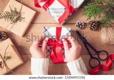 Christmas Background. Female Hands Tying A Red Bow. Woman Packing Christmas Gifts. Holiday Concept. Top View, Flat Lay, Advent Gift