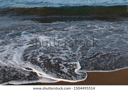 sea background of sandy beach with foam and spray in early summer morning or evening at sunset