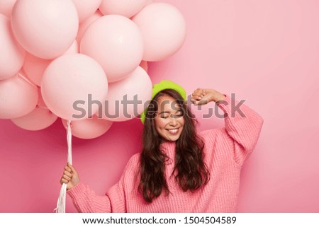 Overemotive chilling woman with cheerful expression, raises hand, dances to music, has fun at party, holds balloons, has happy mood during her birthday. Asian girl celebrates getting new job Royalty-Free Stock Photo #1504504589