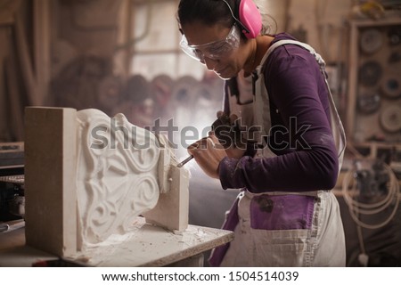Female sculptor working on a piece using hammer and chisel, sculpting a white marble stone into a beautiful pedestal, stonemasonry and stonecraft Royalty-Free Stock Photo #1504514039
