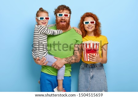 Happy family enjoy film or cartoon in cinema, wear 3d glasses, amused by cool sound and visual effects, eat delicious snack. Small girl on fathers hands, embraces him. People, leisure, weekend