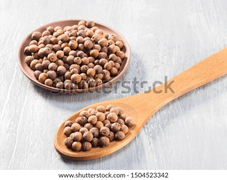 Allspice (Jamaica pepper) in clay plate and wooden spoon diagonally on grey cement background