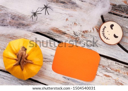 Halloween holiday background with decorations. Flat lay pumpkin, decorative web, spiders, Jack Skellington cookie and blank card on wooden background.
