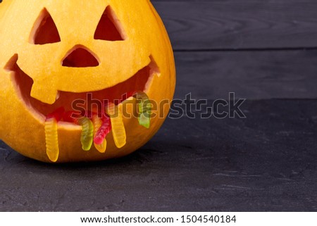 Jack-O-Lantern with gummy worms. Halloween pumpkin on dark background. Funny Halloween decorations.